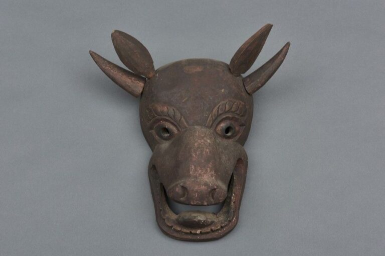 Masque en bois naturel représentant une vache-démon grimaçant la bouche ouvert