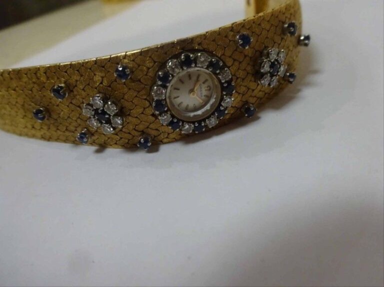 Montre bracelet de dame en or jaune 18K (750°/00) à maillons tissés amatis, orné d'un décor de fleurs serties de diamants taille brillant et de saphirs rond
