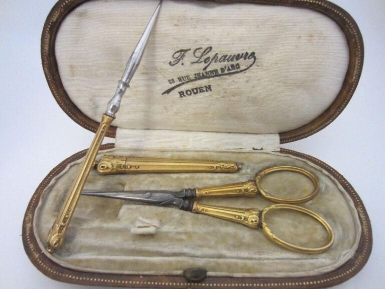 NECESSAIRE A COUTURE en or jaune (750 millièmes) et métal, ciselé de volutes comprenant une paire de ciseaux, un porte aiguilles et un pique Manque le dé à coudre Dans son écrin ovale (usures)