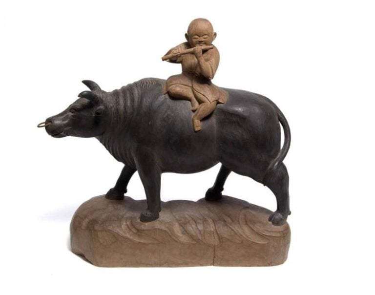 OKIMONO EN BOIS SCULPTE A L'EFFIGIE D'UN GARCON BOUVIER JOUEUR DE FLUTE Japon, Epoque XXe siècle Note : Il s'agit là d'une évocation de la légende - qui trouve sa source en Chine - de l'amour unissant la déesse lune (ou tisserande) et le jeune garçon bouvier, lesquels ne peuvent être réunis qu'une fois l'a