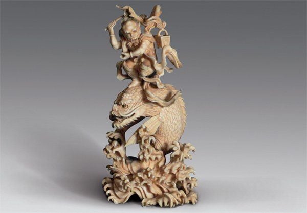 Okimono en ivoire représentant Bunshosei, le démon volant, debout, écharpes au vent, sur une carpe géante à tête de dragon et à nageoires en forme d'aile, jaillissant des flot