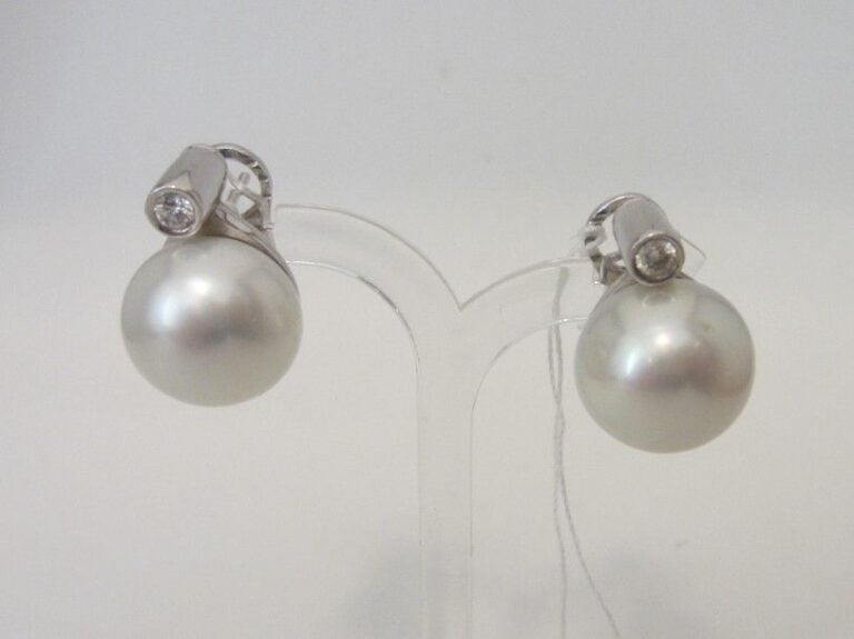 PAIRE de BOUCLES D'OREILLES en or gris (750 millièmes) retenant un perle de culture blanche des Mers du Sud, légèrement bouton, surmontée d'un diamant taille brillant en serti clo