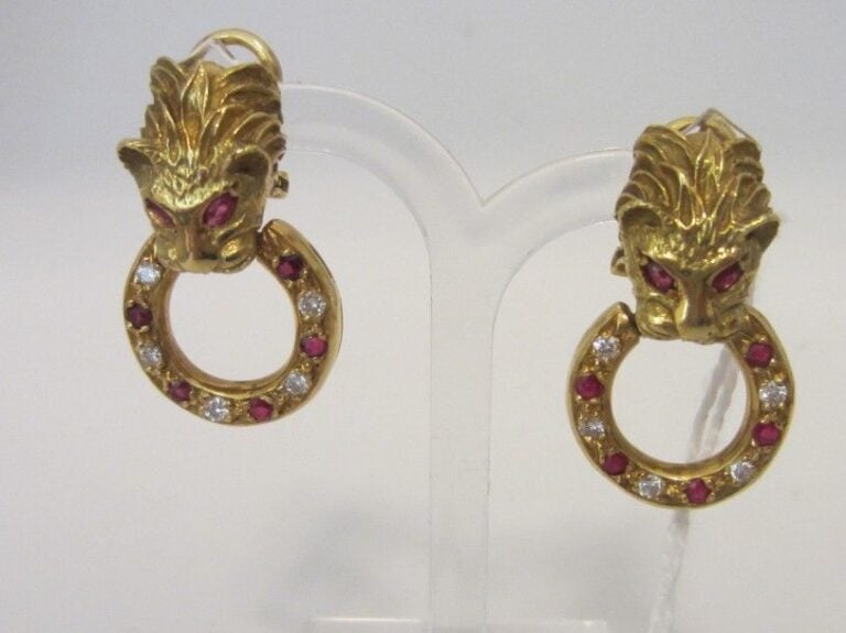 PAIRE de BOUCLES D'OREILLES «panthères» en or jaune (750 millièmes) ciselé et sculpté à motifs de tête de lionne retenant un anneau ajouré serti de diamants alternés de pierres rouge