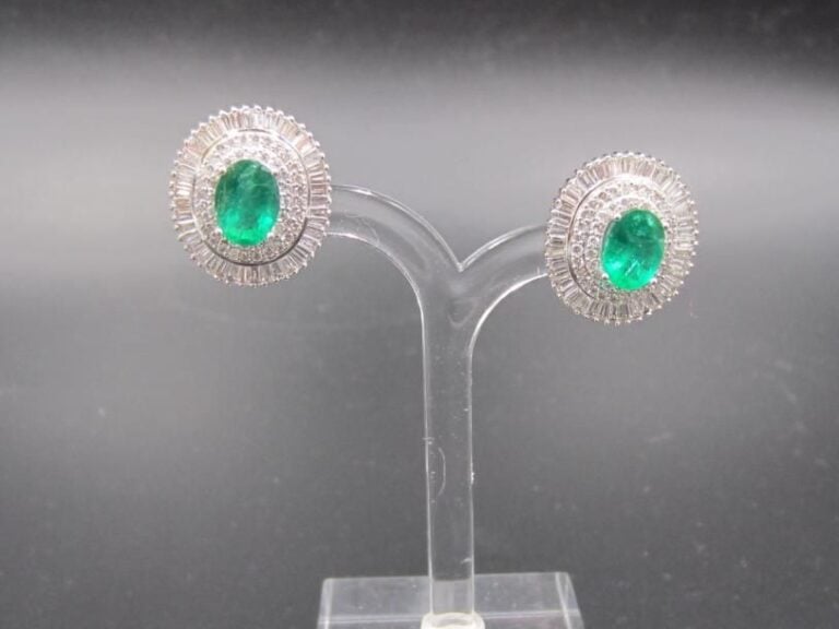PAIRE DE BOUCLES D’OREILLES en or gris (750 millièmes) serti d’émeraudes de forme ovale entourée de deux lignes de diamants taille brillant et baguette