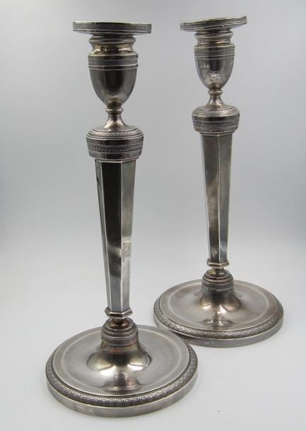 PAIRE DE GRANDS BOUGEOIRS en argent à fûts hexagonaux posant sur une base circulaire à bordure de palmettes; le binet en forme d'urnes à bordure godronnée et motifs gravé