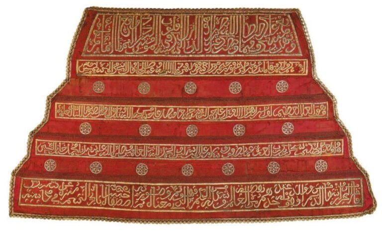 PANNEAU BRODÉ Panneau trapézoïde en velours rouge, brodé aux fils d'argent de cinq bandeaux épigraphiques aux inscriptions coraniques de tailles différentes, quatre d'entre eux séparés par des rosettes inscrites dans des cercle