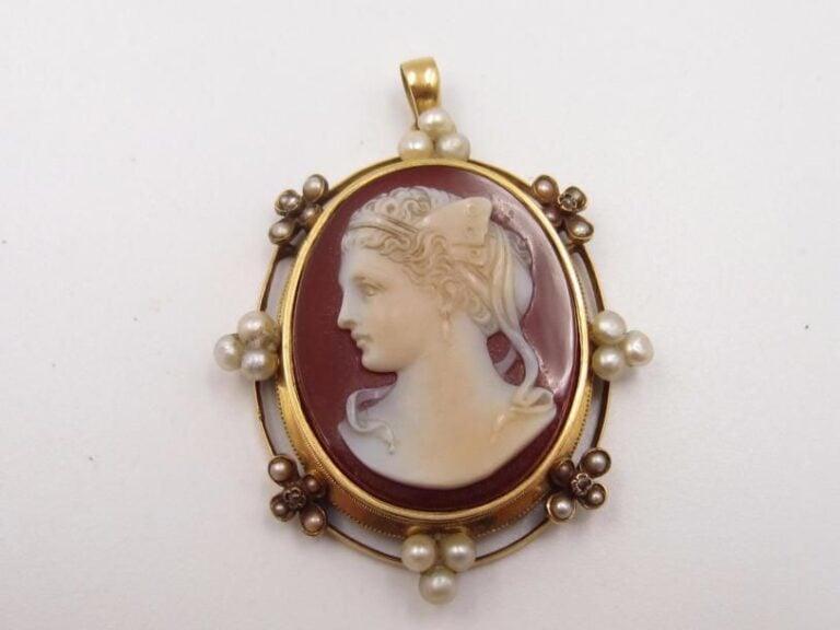 PENDENTIF – PORTE SOUVENIR ouvrant ovale, en or jaune (750 millièmes) ajouré, orné d’un camée en cornaline représentant un « profil de jeune femme » entouré de petites perles blanches et  grises, rehaussées de petits diamants taillés en ros