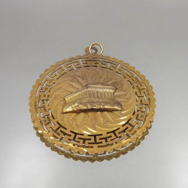 PENDENTIF circulaire en or jaune (375 millièmes) 9 carats, ajouré et ciselé, centré d'un temple de la Grèce antiqu