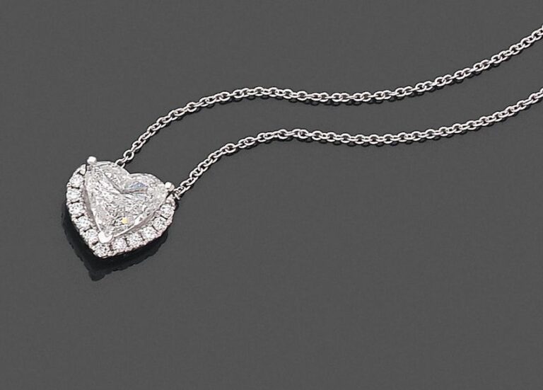 •PENDENTIF «cœur» et sa chaînette en or gris (750‰) serti d'un diamant taillé en cœur pesant 1,89 carat, entouré de diamants taille brillan