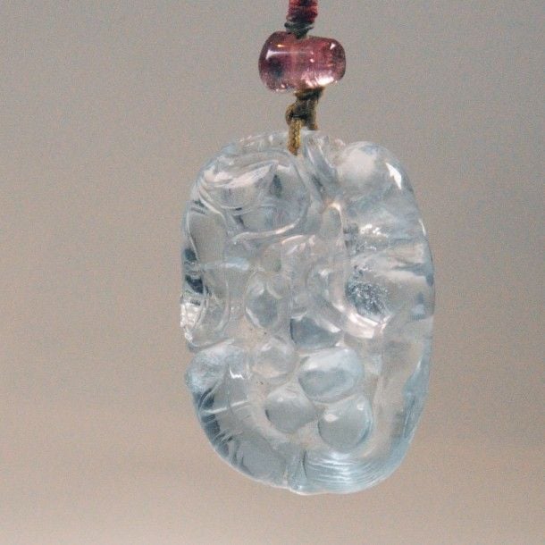 Pendentif en cristal de roche à reflet saphir, sculpté d’un loir sur une grappe de raisin, surmonté d’une perle en tourmalin