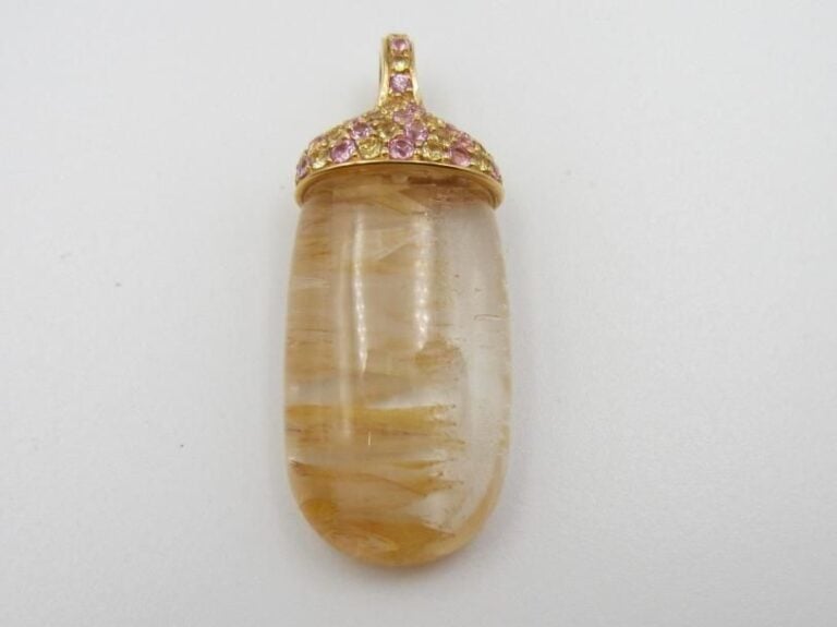 PENDENTIF en or jaune (750 millièmes) serti d’une importante topaze incolore incluse, de forme oblongue surmontée d’un pavage de saphirs roses et jaunes             Long        : 3,7 cm        Poids brut : 11,7 g