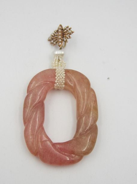 PENDENTIF oblong en tourmaline rose taillée d'un motif cordé, retenu par un ruban de petites perles