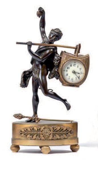 PENDULETTE en bronze doré et patiné figurant un vendangeur traité à l'antique portant un panier dans lequel est inséré le cadran de la pendulette; sur un socle ovale à frise de palmettes reposant sur quatre petits pieds patin