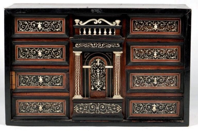 Petit cabinet en placage de bois exotiques; la façade architecturée comporte au centre une galerie à balustre surmontant une colonnade encadrant un tiroir en forme de voute cintrée; de chaque côté, huit tiroirs aux façades à rinceaux d'ivoire sur fond d'ébène encadrés de moulure