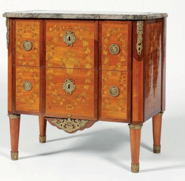 Petite commode marquetée de guirlandes de fleurs et feuilles; au centre, une corbeille chargée de fleurs; de forme rectangulaire, elle ouvre par deux tiroirs sans traverse à ressau
