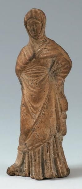 Petite figurine de femme vêtue d'un long himation et emmitouflée dans un grand manteau qu'elle retient au niveau du co