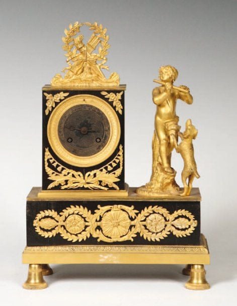 Petite pendule en placage d'ébène et bronze ciselé doré à décor d'un pâtre jouant de la flûte devant son chien symbolisant la fidélité ; décor des attributs de l'amou
