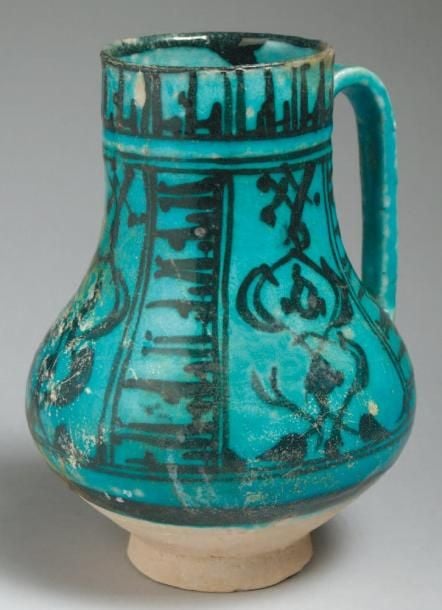 PICHET AUX BANDEAUX COUFIQUES Pichet piriforme à anse verticale, décoré en noir sous glaçure turquoise de bandeaux verticaux d'inscriptions coufiques séparés par des palmettes entrelacée
