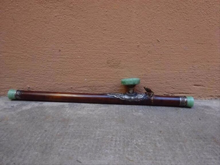 PIPE A OPIUM EN BAMBOU ET A EMBOUTS ET FOYER A L'IMITATION DU JADE JADEITE Chine, Epoque XXe siècle La monture en métal argenté à décor d'une perle enflammée ; les bagues de même aux symboles du couple impérial: dragon et phénix affrontés (fêles, griffures