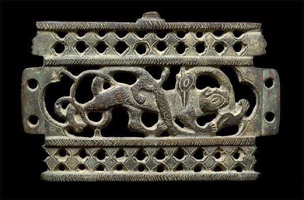 PLAQUE DE BRASERO Plaque en bronze ajourée, percée de quatre trous latéraux et bordée de chevrons gravés et de deux frises de fleurons encadrant une lionne et un oiseau fantastique s'entredévoran