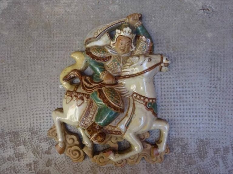 PLAQUE DECORATIVE / TUILE EN GRES EMAILLE POLYCHROME FORMANT CAVALIER République Populaire de Chine ou Koji Kochin de Taiwan, Seconde moitié du XXe siècle Elle représente un cavalier chevauchant sa monture lancée au galop sur des volutes nuageuses, son sabre- qu'il tient de la main gauche - brand