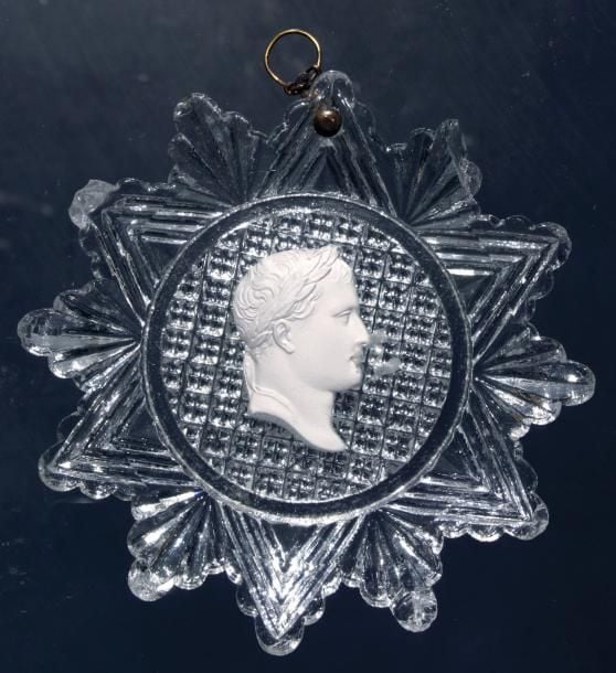 Plaque en cristal moulé à bord dentelé et revers guilloché, orné d'un cristallo-cérame représentant le profil lauré de l'empereur Napoléon 1er (éclat et égrenures