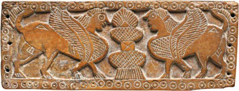 PLAQUE EN OS Plaque rectangulaire percée de trous sur les côtés, décorée en léger relief de deux sphinges ailées affrontées de part et d'autre d'un arbre de vie à palmett