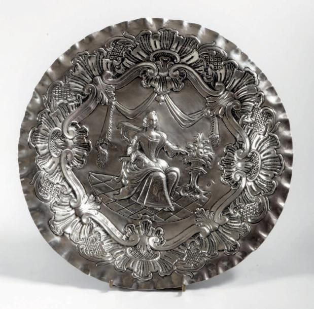 PLAT DE DÉCORATION en argent à décor en repoussé d'une femme assise près d'une vasque de fleurs dans un entourage de draperie, coquilles rocailles et agrafes d'acanth