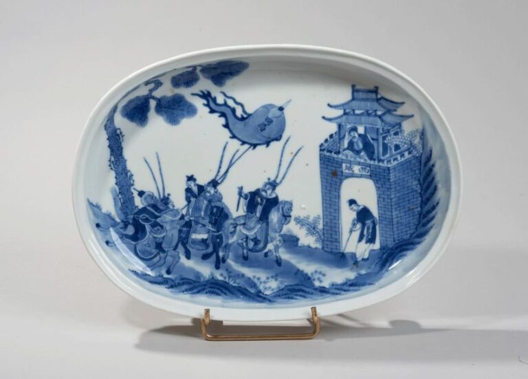 Plat ovale quadripode en porcelaine à décor en bleu sous couverte de guerriers au pied d'une muraill