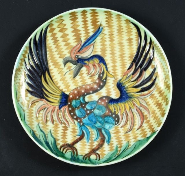 Plat rond en faïence fine à décor polychrome d'oiseau fantastique sur fond jaune à bandes losangées brune