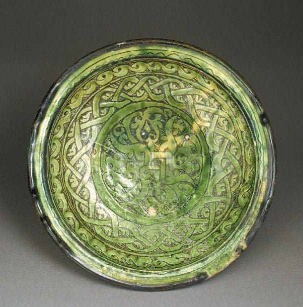 PLAT TRIPODE Petit plat tripode, décoré d'entrelacs et de lignes sinusoïdes et concentriques sur le rebord, gravés sous glaçure vert