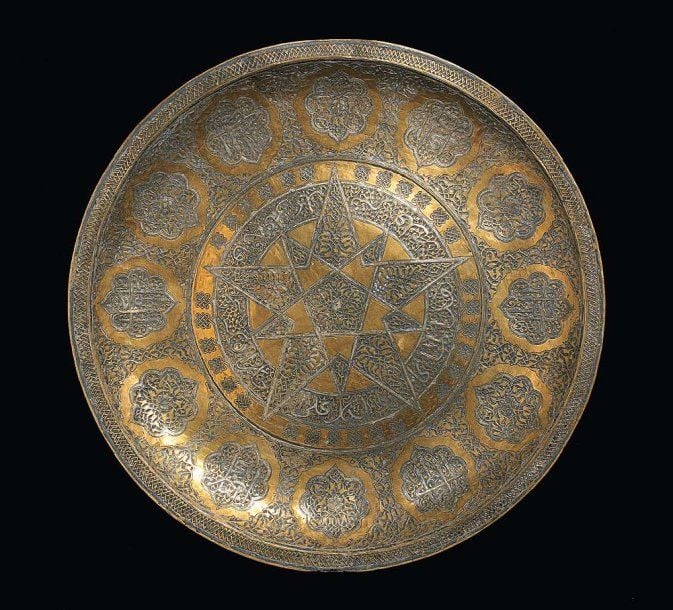 PLATEAU Grand plateau discoïde à rebord plat, en cuivre incrusté gravé et incrusté d'argent, décoré d'une rosace étoilée, entourée de douze médaillons polylobés tapissés d'entrelacs ou d'inscription
