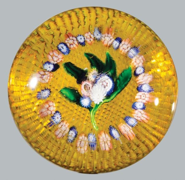 Presse-papiers à fond ambre guilloché orné d'un bouquet composé de cinq bonbons polychromes organisés sur cinq feuilles vertes, entouré d'une couronne de bonbons roses et blancs alternés de bonbons bleus et blanc