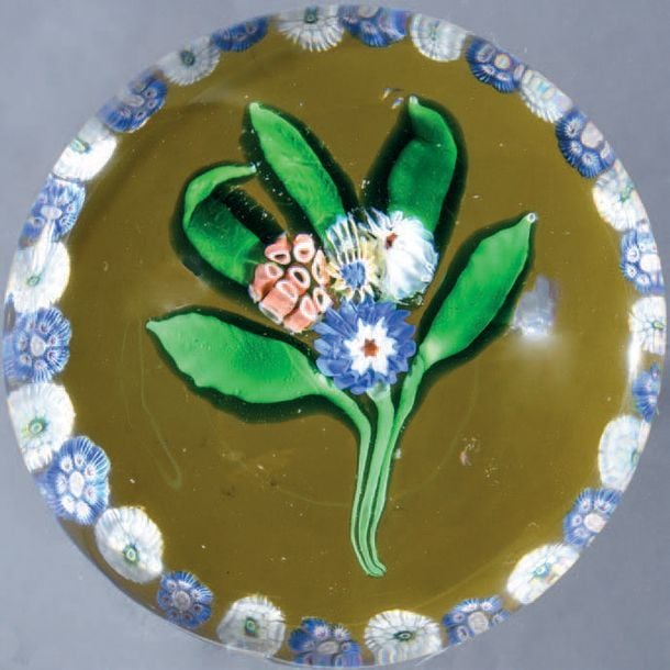Presse-papiers à fond ambre orné d'un bouquet composé de quatre bonbons polychromes sur cinq feuilles vertes; couronne de bonbons blancs alternés de bonbons bleu clair et blancs à fléchettes noire
