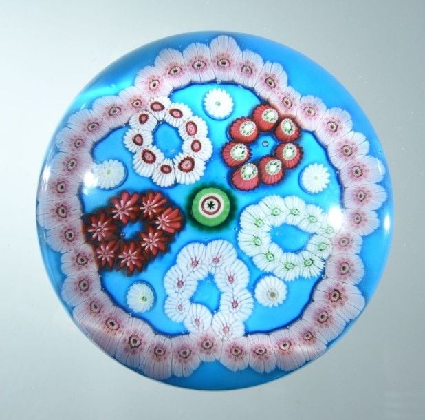 Presse-papiers à fond bleu clair doublé sur blanc orné d'une rosace formée de cinq motifs circulaires formés de bonbons polychromes séparés par cinq bonbons blancs et entourés par une couronne de bonbons blancs et roses; bonbon central vert, blanc et roug