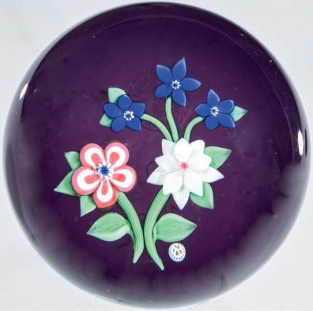 Presse-papiers «Composition champêtre», signé et daté B 1982, à fond violet translucide orné d'un bouquet composé d'une primevère rouge et blanche, d'une double clématite blanche et de trois fleurettes bleue