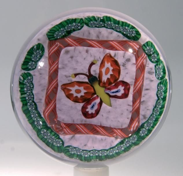 Presse-papiers en verre rose et fond blanc orné d'un papillon à corps jaune et ailes oranges et blanches, encadré par une torsade orange et blanche en losange et un cercle périphérique de bonbons verts et blanc