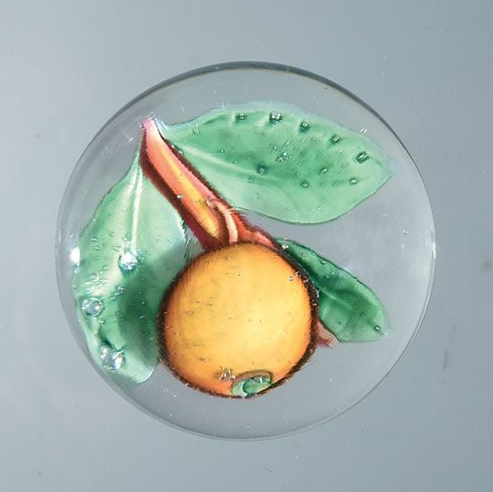 Presse-papiers orné d'une pomme orangée, sur une tige ocre portant trois feuilles vert tilleu