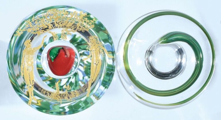 Presse-papiers Tentation, signé et daté SL 2003, composé de deux demies sphères, l'une à fond jaspé vert, blanc et bleu, la face intermédiaire à motif gravé et doré représentant Adam et Ève de part et d'autre d'un pommier; la partie supérieure ornée d'un serpent vert lové; la cavité centrale recèle une pomme en cristal émaillé roug