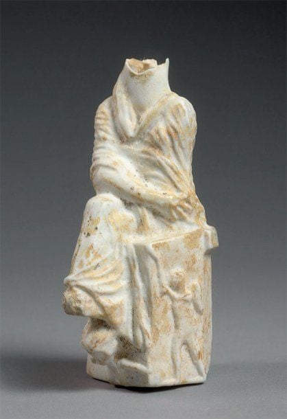 RARE FLACON ANTHROPOMORPHE Flacon blanc acéphale représentant une femme (Tyché) au vêtement drapé, assise, un bras plié vers la hanche, sur un siège polygonal décoré d'un Eros, d'un arc et d'un carquoi