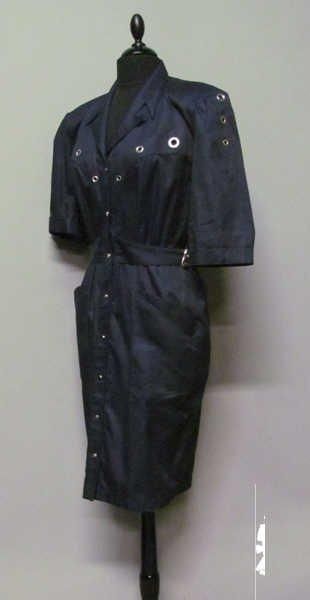ROBE-CHEMISE en sergé de coton marine ornée d'oeillets en métal argenté, court col cranté sur simple boutonnage pressions jusqu'au bas de la jupe droite, petites manches à revers, taille soulignée d'une ceinture à même incurvée s'attachant à l'aide de boucles à ardillons de chaque côté, deux poches plaquées (griffe bleue, graphisme argent) (env TM)