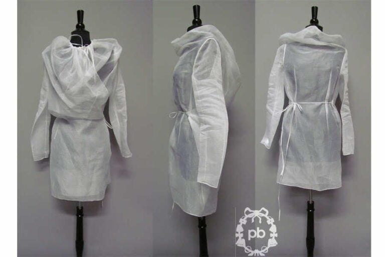 ROBE-TABLIER déstructurée en gaze transparent blanc s'attachant à l'aide de liens à la taille ainsi qu'à l'encolure coulissée (griffe blanche, graphisme noir et rouge) (env TM) (mini accro)