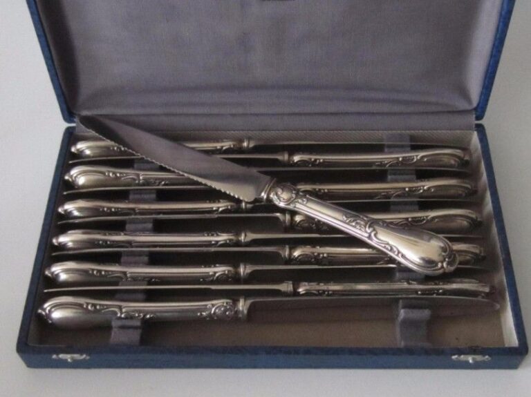 Série de 12 couteaux de table, manches en argent fourré à décor de feuillages et coquilles stylisées ; lames crantée