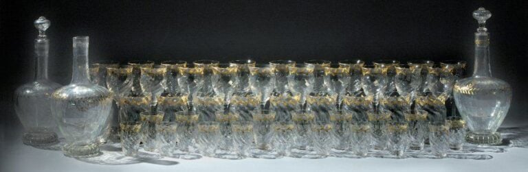 Service de verres en verre blanc transparent à décor de frise feuillagée à l'or se composant de 50 verres de formes et de tailles différentes et de 3 carafes dont une sans bouchon (petits éclats et légers effacement de dorure