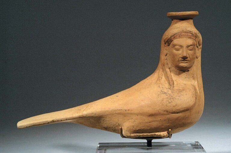 SIRÈNE Aryballe en terre rouge, à corps d'oiseau et tête féminine tournée de côté, ceinte d'un diadème, surmontée d'un col de récipien