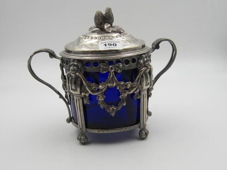 Sucrier couvert en argent ajouré de pilastres à mufles et pattes de lion, guirlandes de fleurs et frise d'oves; les anses ajourées à motif de feuilles; le couvercle gravé de guirlandes feuillagées, noeuds de rubans et chiffré; le frétel figurant deux fraises et leur feuillag