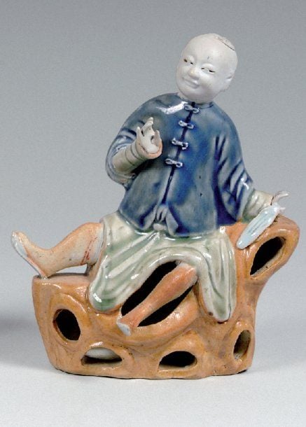 Sujet en biscuit émaillé bleu, céladon et jaune, représentant un jeune homme assis sur une roche percée, tenant un morceau d'étoff