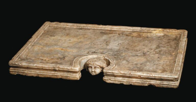 TABLE Table rectangulaire en albâtre, bordée de cannelures, et dont l'encoche centrale est ornée d'une tête sculptée en ronde boss