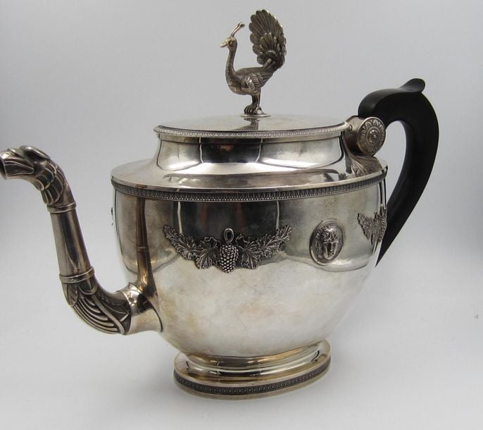 THÉIÈRE ET POT À LAIT en argent uni (950 millièmes); la théière sur bâte à décor d'oves; la panse ornée de deux mascarons et de grappes de raisin en relief et d'une frise de feuilles d'ea
