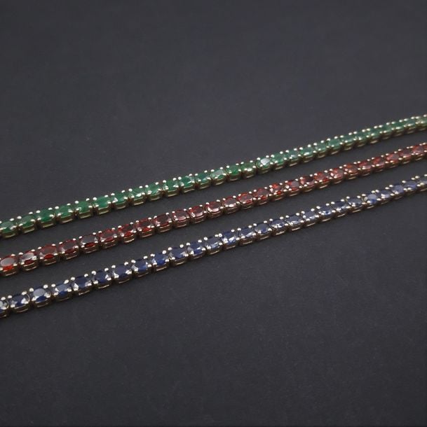 Trois BRACELETS en vermeil (925 millièmes) serti respectivement d'un alignement de grenats, émeraudes et saphirs, de forme oval